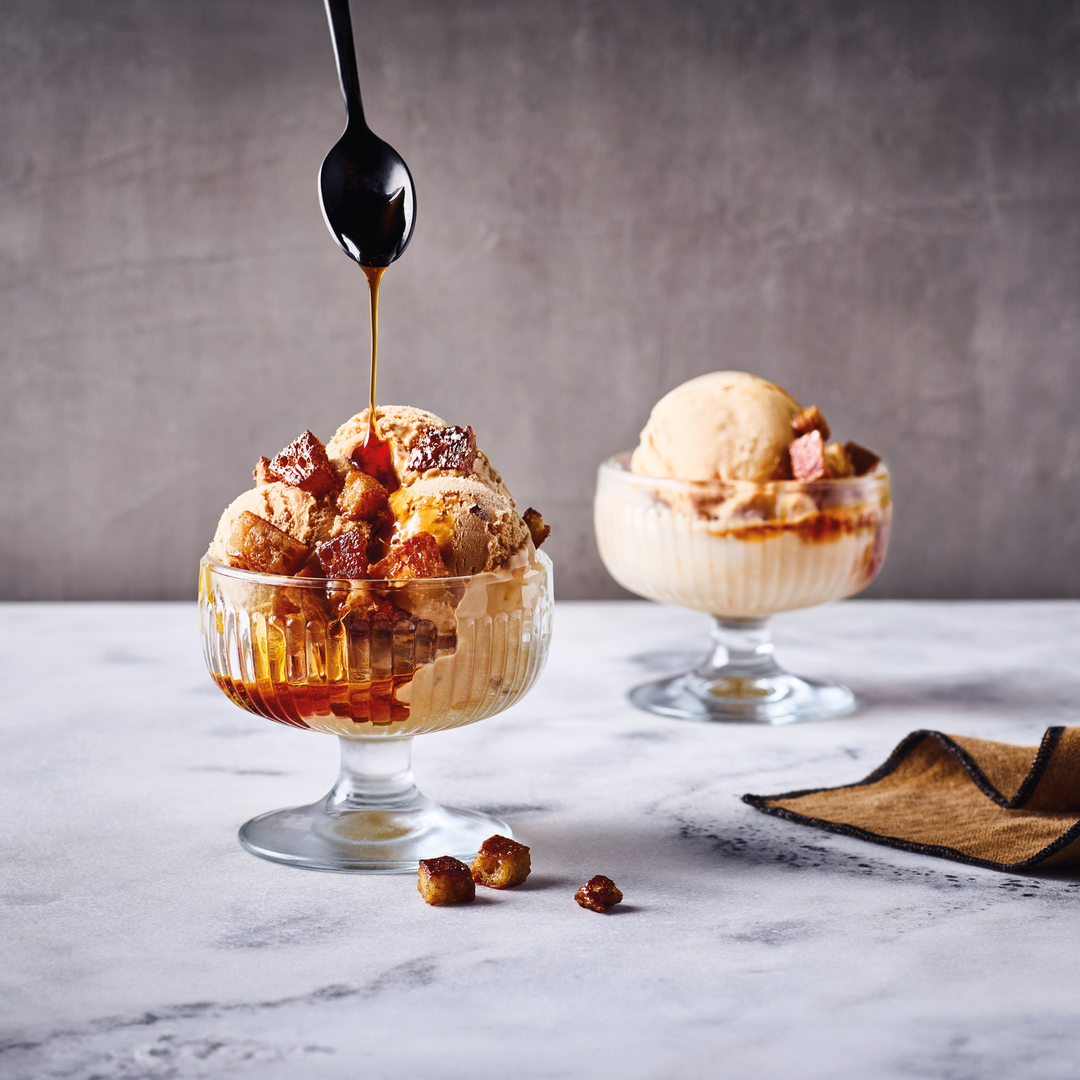 Two dessert glasses with ice cream and caramel sauce on a marble surface.